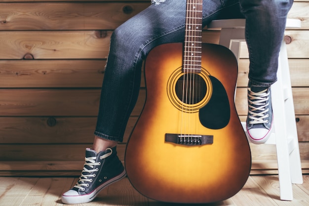 Acoustic guitar and legs of female sitting on stool in jeans