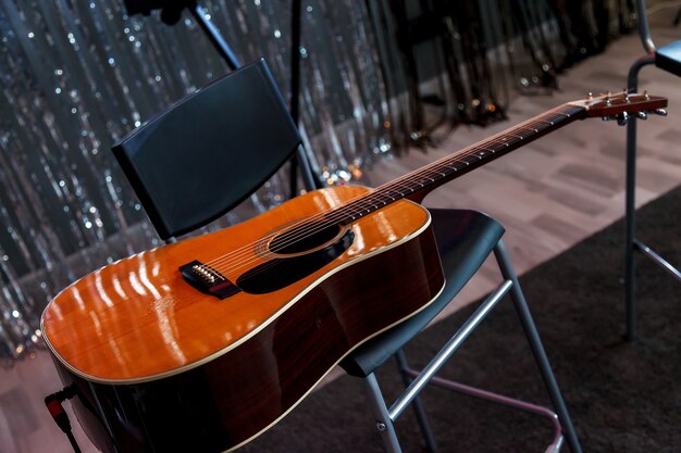 Chitarra acustica su poltrona in plastica all'interno di uno studio contemporaneo. la chitarra acustica si trova sul nero davanti allo sfondo della parete di orpelli lucidi. tempo per hobby e svago. copia spazio per il sito