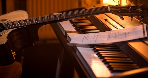 acoustic guitar stands on piano with notes, close-up