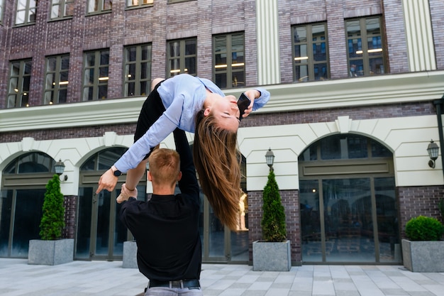 Acro yoga position of young couple, man hold woman up by leg and torso, and woman talk by smartphone, exercise about trust and support and business concept