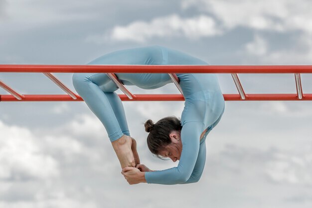 Foto ragazza dell'acrobata in un vestito blu su una barra orizzontale