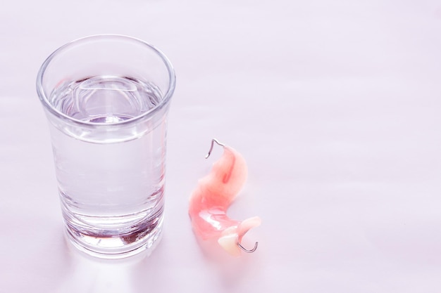 Acrylic dentures immersed in a glass of watertable in the bedroom Bright simple background