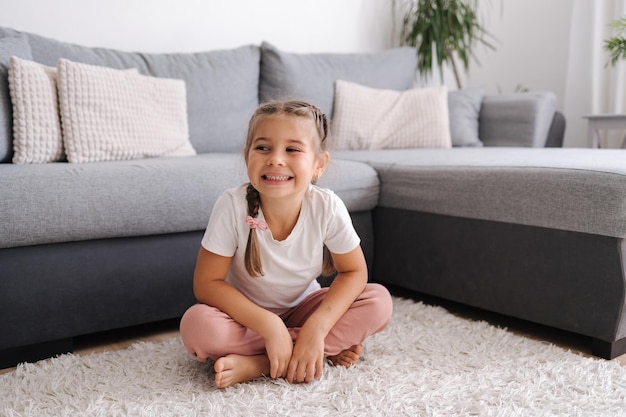 Actief en energiek klein meisje hebben plezier en thuis woonkamer kind zit op het tapijt