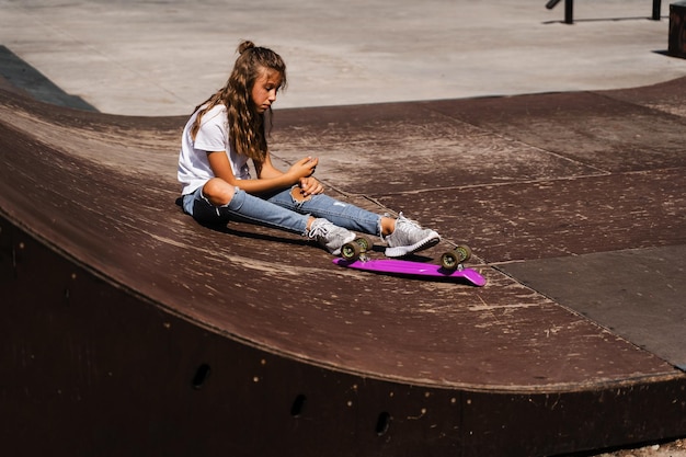Foto actief kindmeisje na val van pennyboard gewond zittend en voel pijn op sporthelling op skateparkspeeltuin