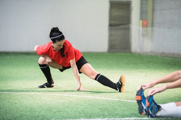 Actief meisje in sportuniform doen oefening voor het strekken van benen op voetbalveld tijdens het trainen voor de wedstrijd