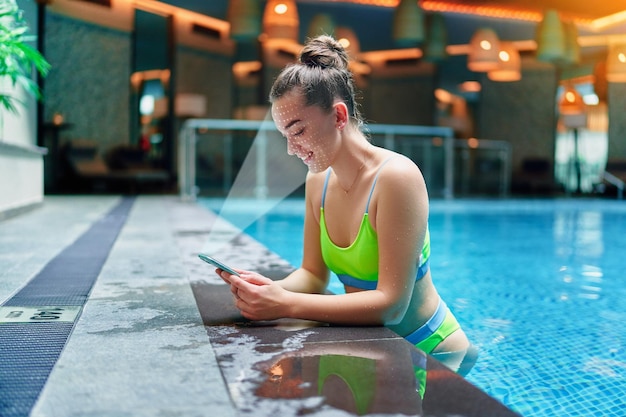 Actieve atletische vrouw scant het gezicht met behulp van gezichtsherkenningssysteem voor het ontgrendelen van de telefoon tijdens het trainen in het zwembad van het spa-fitnesscentrum