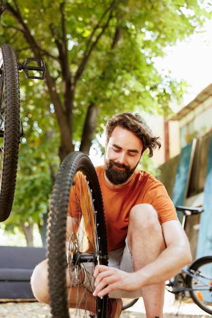 Actieve en toegewijde man gehurkt om de velg van het fietswiel in de tuin te repareren met behulp van professionele tool. Gezonde mannelijke fietser die buiten aan een gedemonteerde fietsband werkt met behulp van een gespecialiseerde sleutel.