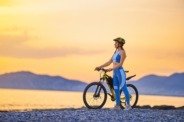 Actieve jonge fitnessvrouw met sportkleding en helm die alleen staat met de fiets buiten