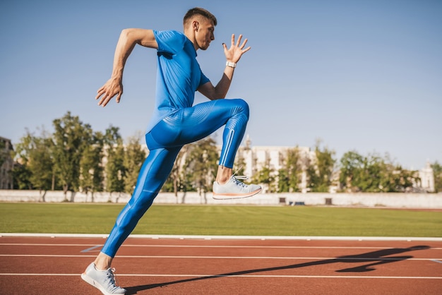 Actieve jonge mannelijke atleet rennen en joggen alleen langs een racebaan in het stadion terwijl hij traint voor de marathon op een zonnige dag Sport levensstijl en mensen concept