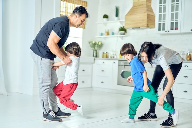 Actieve latijnse ouders van middelbare leeftijd die twee kleine jongens 's ochtends oefeningen laten doen. gezonde levensstijl. spaanse familie die thuis aan het trainen is