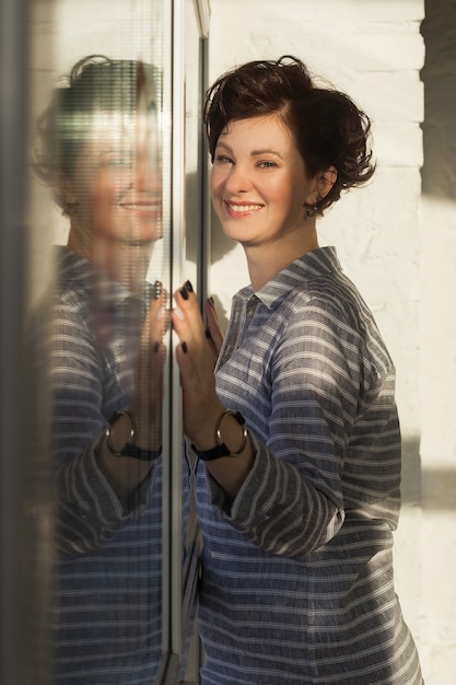 actieve, mooie vrouw van middelbare leeftijd met een mooie glimlach. Zittend op de vensterbank bij het raam. Reflectie in het raam.