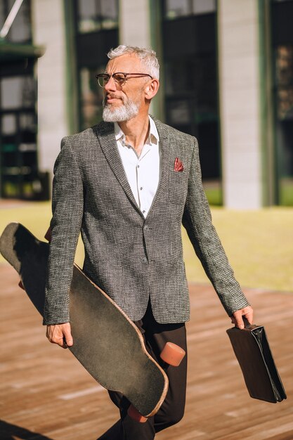 Actieve rust. Een zakenman die met een skateboard in handen loopt