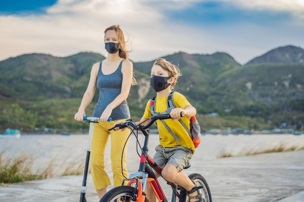 Foto actieve schooljongen en zijn moeder in een medisch masker fietsen met een rugzak op een zonnige dag gelukkige kind fietsen op weg naar school je moet met een masker naar school gaan vanwege de coronavirus-epidemie