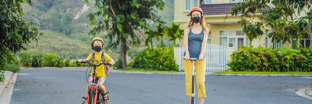 Actieve schooljongen en zijn moeder met medisch masker en veiligheidshelm op een fiets met rugzak op