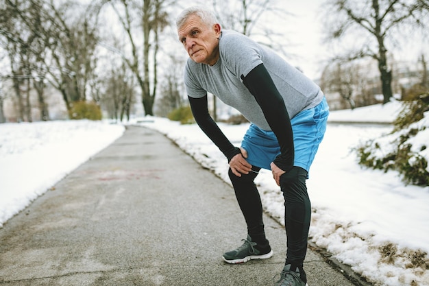 Actieve senior die pauzeert tijdens het joggen en oefeningen doet in het openbare park tijdens de wintertraining buiten naar binnen. Kopieer de ruimte.