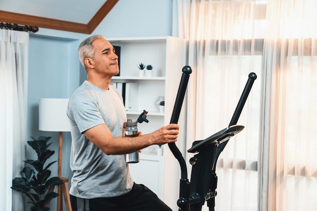 Foto actieve senior man draait op elliptische loopmachine en drinkwater thuis portret als fitness gezonde levensstijl en lichaamsverzorging na pensionering voor gepensioneerde clout