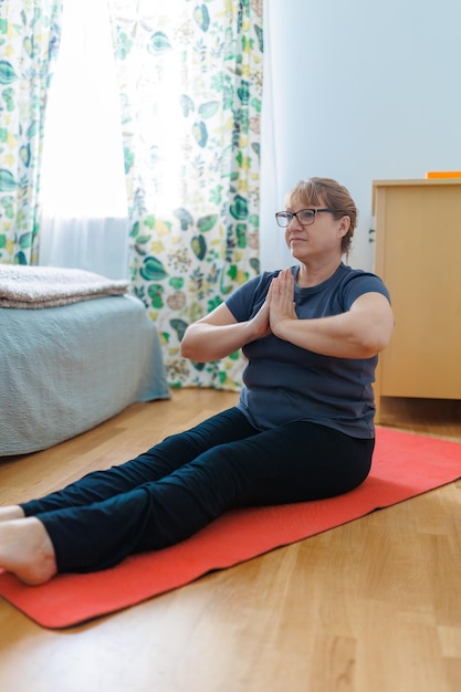 Actieve senior vrouw doet buikspieroefeningen op yogamat thuis en glimlacht naar de camera