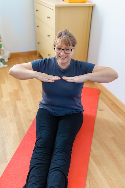 Actieve senior vrouw doet buikspieroefeningen op yogamat thuis en glimlacht naar de camera