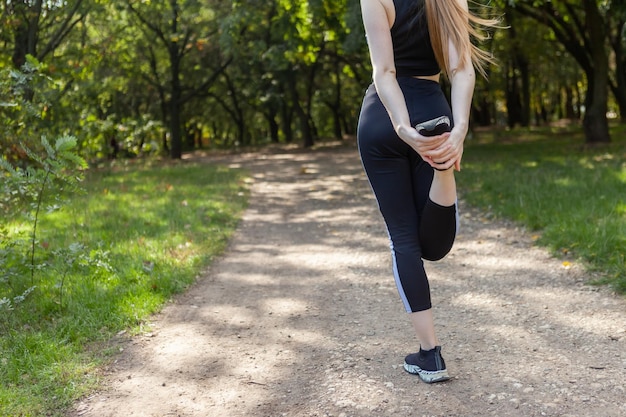 Actieve, slanke vrouw loper in sportkleding strekt haar benen uit in het park gezonde levensstijl