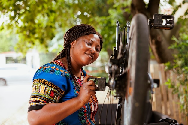 Actieve sportieve afro-amerikaanse vrouw onderhoudt en repareert fietsonderdelen buiten met behulp van gespecialiseerd gereedschap. Vrouwelijke fietser die met enthousiasme een beschadigde fiets nauwgezet inspecteert en repareert.