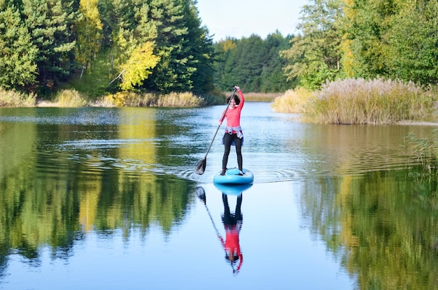Actieve vrouw peddelen SUP board op prachtig meer, herfst boslandschap en natuur op de achtergrond