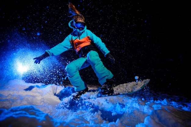 Actieve vrouwelijke snowboarder gekleed in een oranje en blauwe sportkleding springen op de berghelling