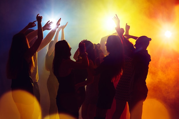 Acting. A crowd of people in silhouette raises their hands on dancefloor on neon light background. Night life, club, music, dance, motion, youth. Yellow-blue colors and moving girls and boys.