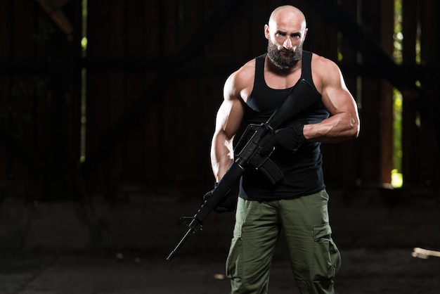写真 緑のズボンを身に着けている廃墟の建物に立っている機関銃を保持しているアクションヒーロー筋肉質の男
