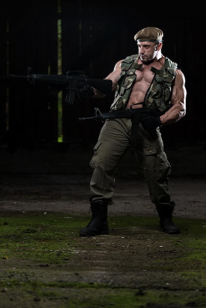 Action Hero Muscled Man Holding Machine Guns  Standing In Abandoned Building Wearing Green Pants