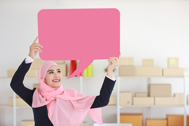 Active asian muslim woman in blue suit standing and holding pink speech bubble