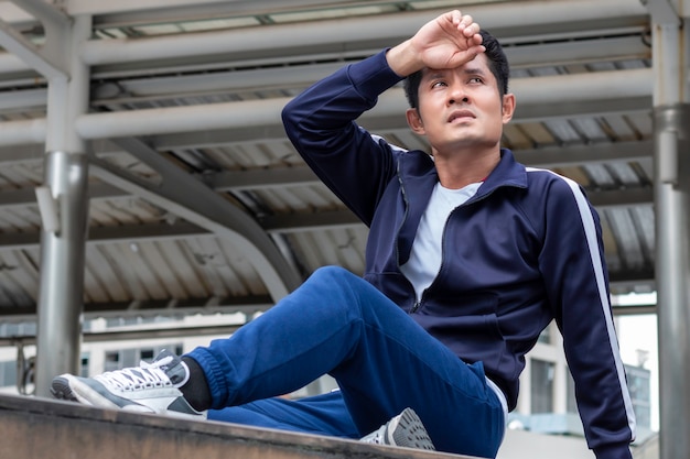 Photo active asian young man tired and resting during exercise on street outdoor.