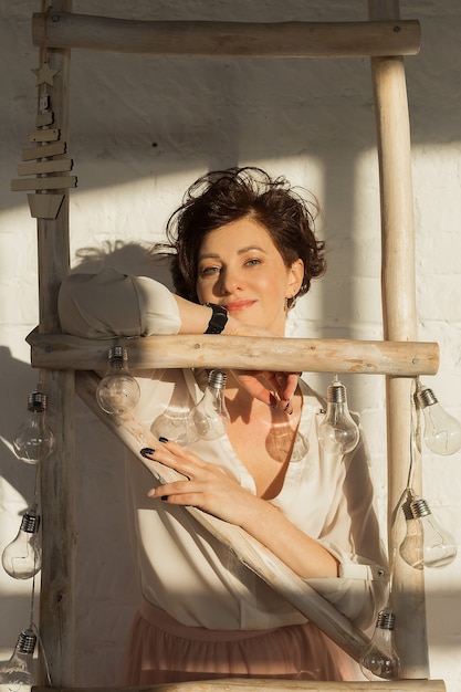  active, beautiful middle-aged woman. Close-up of a woman's face with a smile. Holding onto a ladder with light bulbs