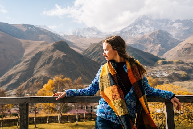 暖かいジャケットを着たアクティブな美しい少女は、雄大な山々を背景に立って、自然ときれいな空気を楽しんでいます