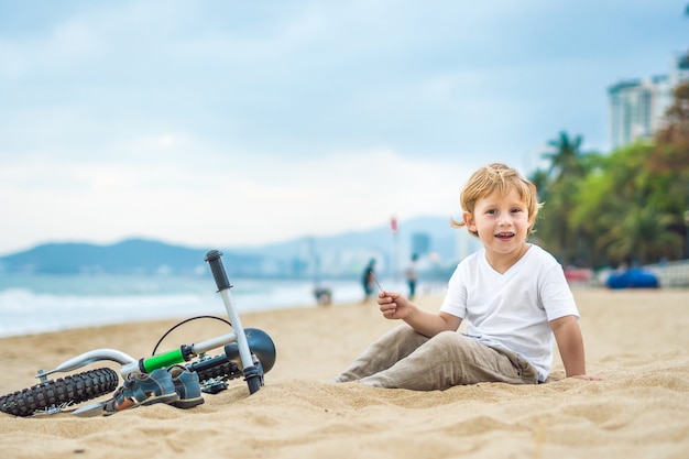 Active blond kid boy driving bicycle in the park near the sea