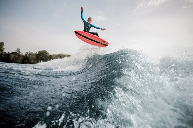 Active boy dressed in black and blue swimsuit surfing jumping up on orange board