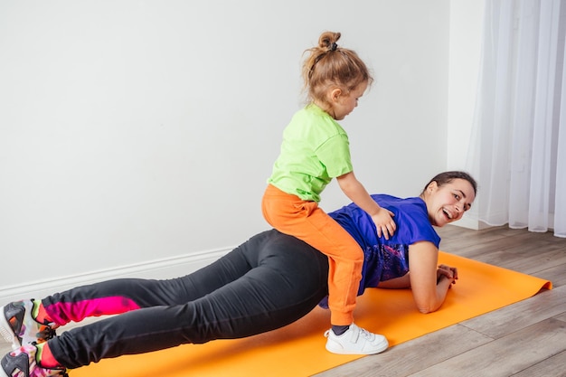 Active boy laying on his mother while she is standing in plank