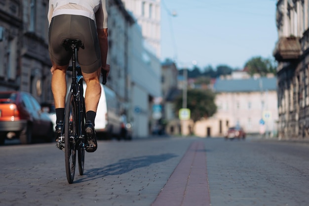 スポーツ服とスニーカーでアクティブな白人男性が街の通りをサイクリング屋外で自転車に乗っている筋肉質の男性の脚のクローズアップアクティブなライフスタイル