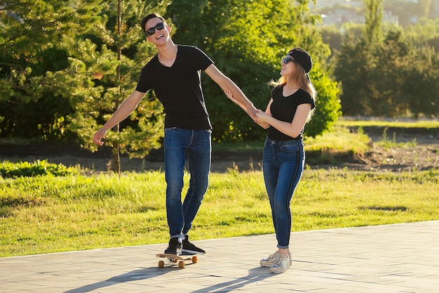 Active couple in love sport skating in the summer park.\
beautiful woman and man have fun with skateboard(longboard)\
background the river. guy and girl date. active lifestyle among\
young people