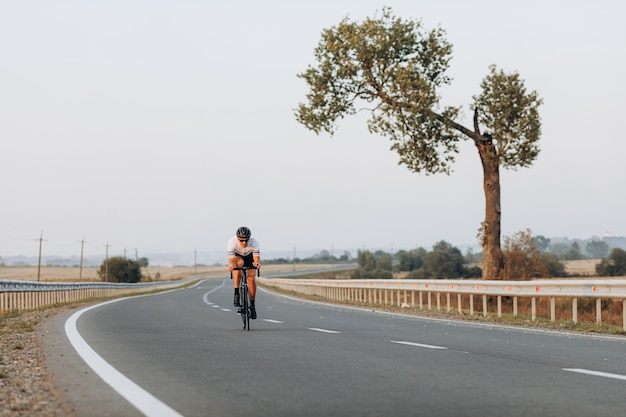 舗装道路でのトレーニングに自転車を使用してスポーツウェアと保護ヘルメットを着用しているアクティブなサイクリスト