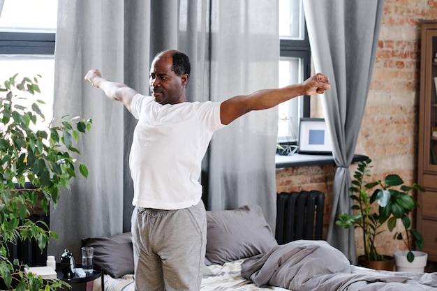 Active elderly black man with outstretched arms exercising in the morning