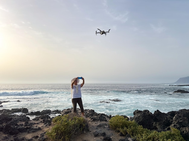 Active elderly woman on a rocky beach takes photos of the drone flying above her