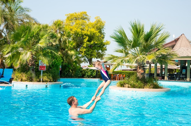 Active father teaching his kid daughter to swim in pool on tropical resort Summer vacations and sport concept