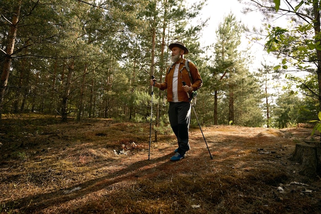 Active fit elderly man having walk using nordic poles outdoors