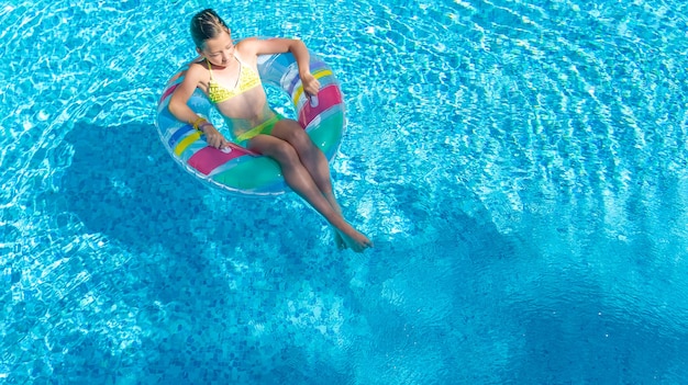 Active girl in swimming pool aerial top view from above, kid swims on inflatable ring donut , child has fun in blue water