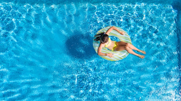 Active girl in swimming pool aerial top view from above, kid swims on inflatable ring donut