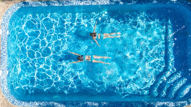 Active girls in swimming pool water aerial drone view from above, children swim, kids have fun on tropical family vacation, holiday resort concept