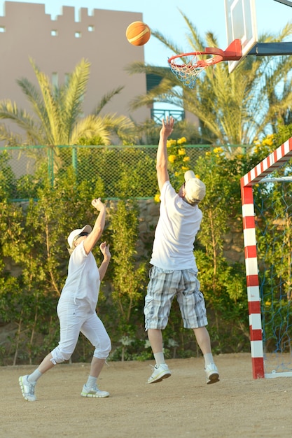 Активная счастливая старшая пара играет в баскетбол на открытом воздухе