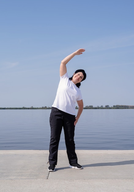 Active and happy senior woman exercising near the riverside