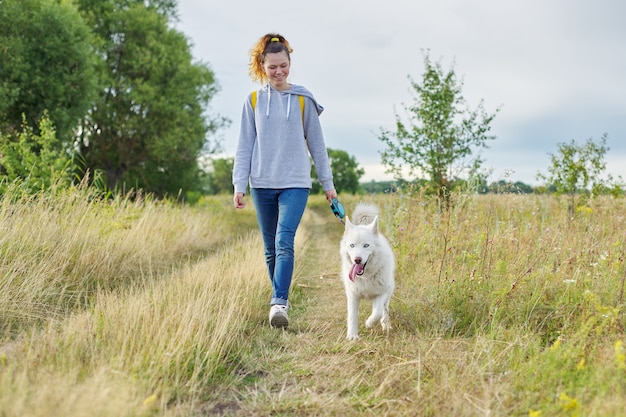 アクティブな健康的なライフスタイル、白いハスキー犬と一緒に歩く十代の少女