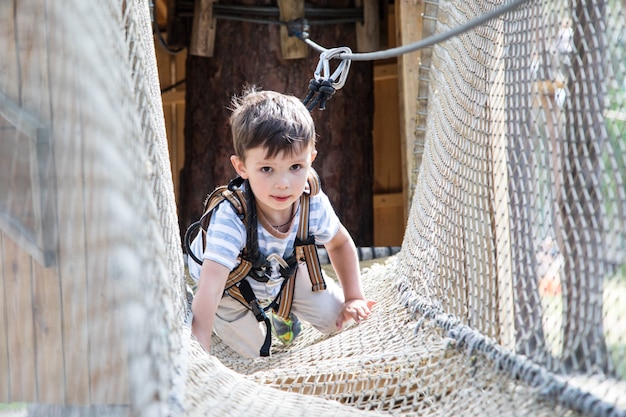 クライミングネットで遊ぶアクティブな小さな子供。子供たちは晴れた夏の日に屋外で遊びそして登ります。